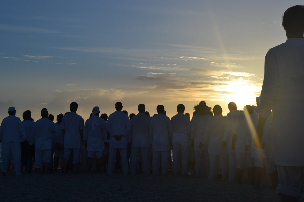Corrente mediúnica vestida de branco na praia ao pôr do sol